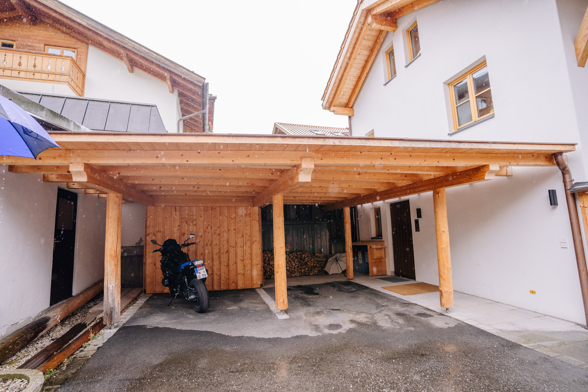 Carport aus Holz: Welche Holzarten sinnvoll sind A wooden carport attached to a modern house, sheltering a motorc