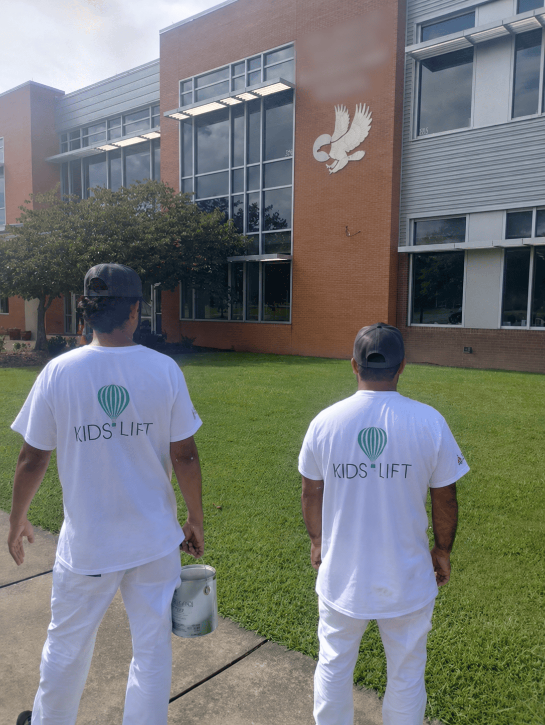 Two 360 Painting of Little Rock team members in Kids Lift shirts carrying paint toward a school building