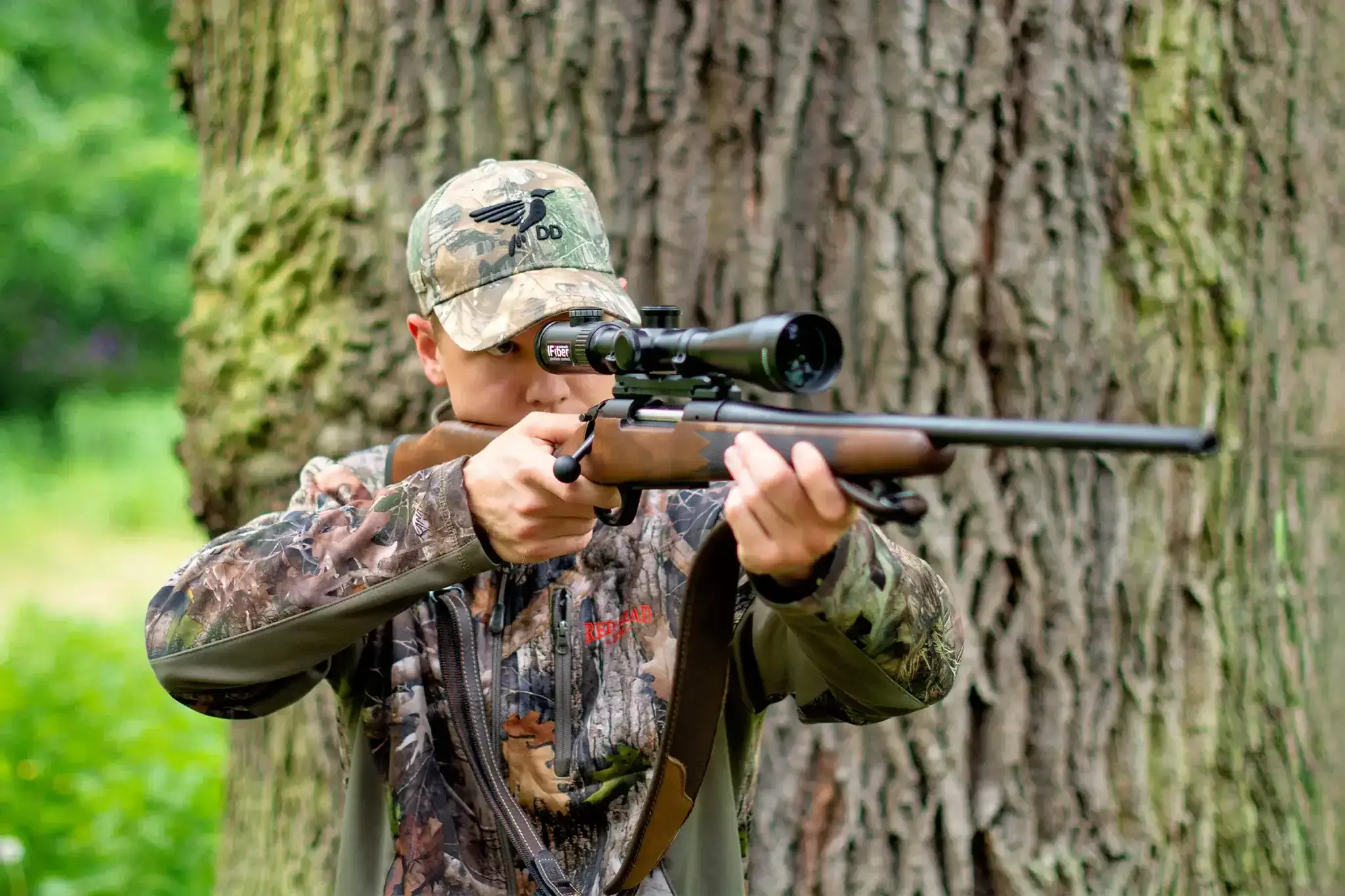 Jäger mit Jagdgewehr im Anschlag im Wald – optimales Setup für Sau, Reh, Hirsch und Fuchs