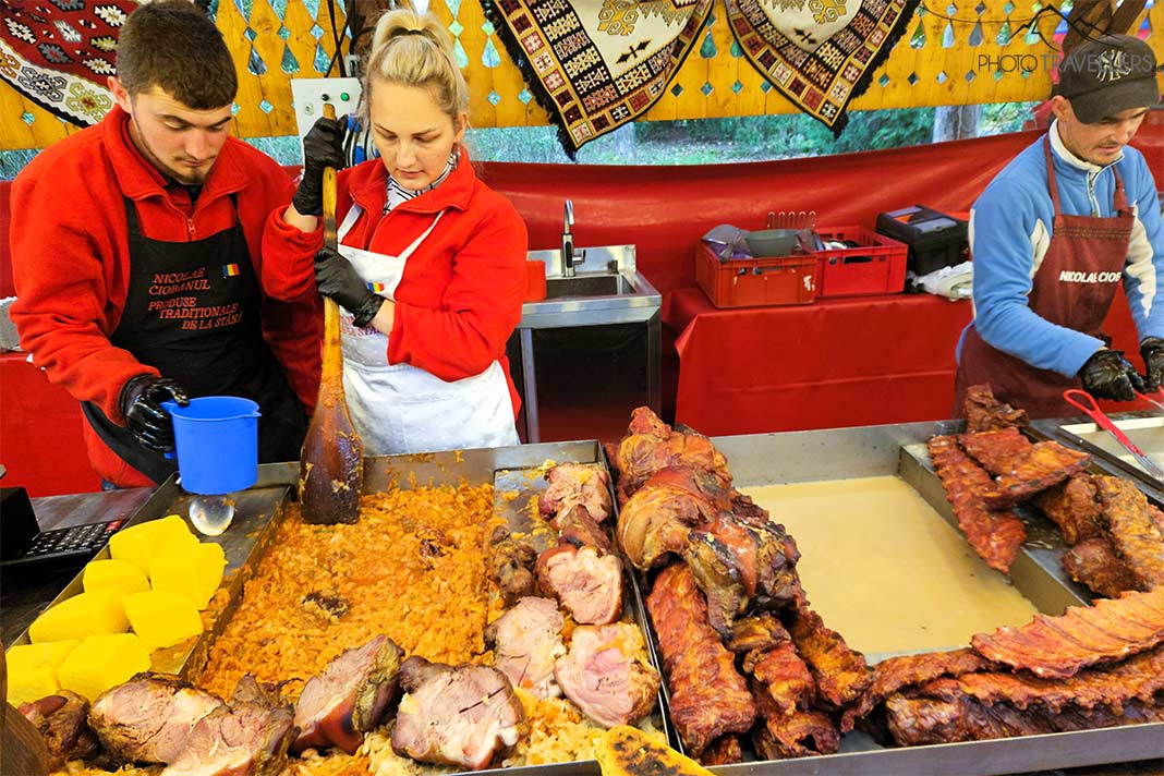 Eine blonde Frau und ein Mann mit Mütze stehen hinter einem Marktstand mit verschiedenem Fleisch