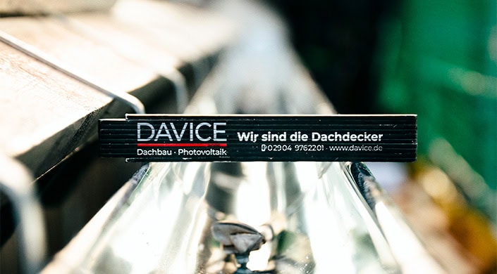 Schwarzes Schild mit weißer Aufschrift „Wir sind die“ und teils sichtbarer Telefonnummer, unscharfer Hintergrund mit metallischen und reflektierenden Oberflächen.