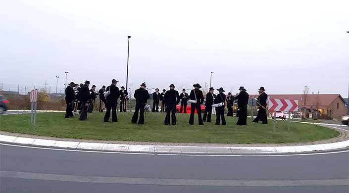 Eine Gruppe von Menschen in traditioneller Zunftkleidung steht auf einer Wiese unter freiem Himmel zusammen.