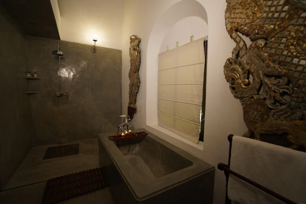 A vintage bathroom featuring a dragon mural, a bathtub with a candle holder, and ornate taps in Adigar's manor Peacock Royal room.