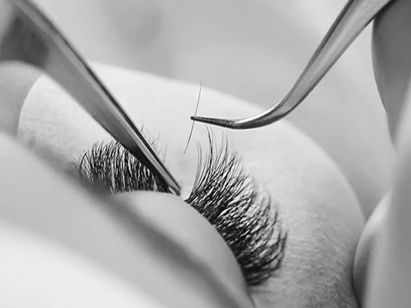 Detailaufnahme einer Wimpernverlängerung mit Pinzette und künstlichen Wimpern.