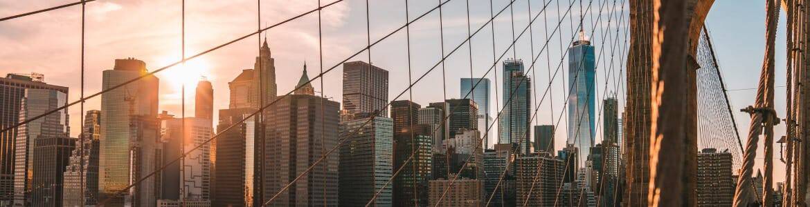 Sunset over the Manhattan skyline seen through the Brooklyn Bridge's iconic suspension cables.