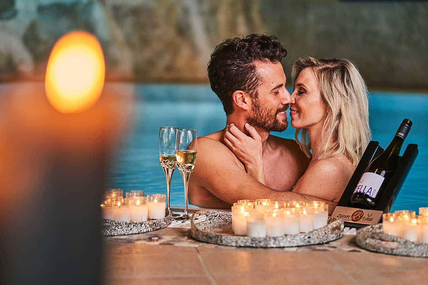 Ein Paar küsst sich am romantisch dekorierten Innenpool - ein Special unseres Wellnesshotel