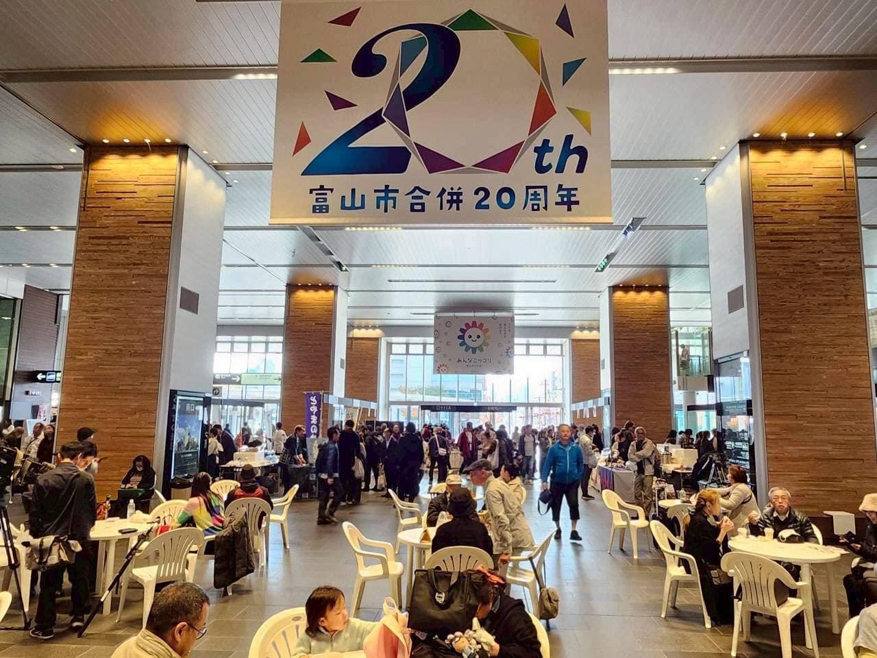 富山駅が巨大な寿司ストリートに!?すしフェスティバル2025出演レポート 5 富山市合併20周年のバナーが掲げられた富山駅南北自由通路のイベント会場と、多くの来場者で賑わう様子