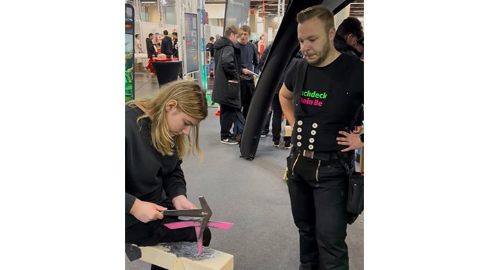 Mehrere Menschen unterhalten sich auf einer Messe oder Ausstellung, während eine Person im Vordergrund arbeitet.