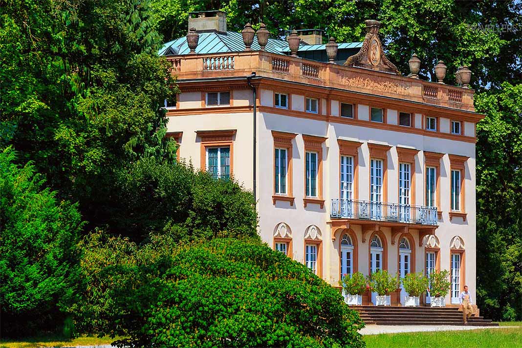 Das beigefarbene Rokoko-Schloss Schönbusch ist eingebettet in üppiger Natur