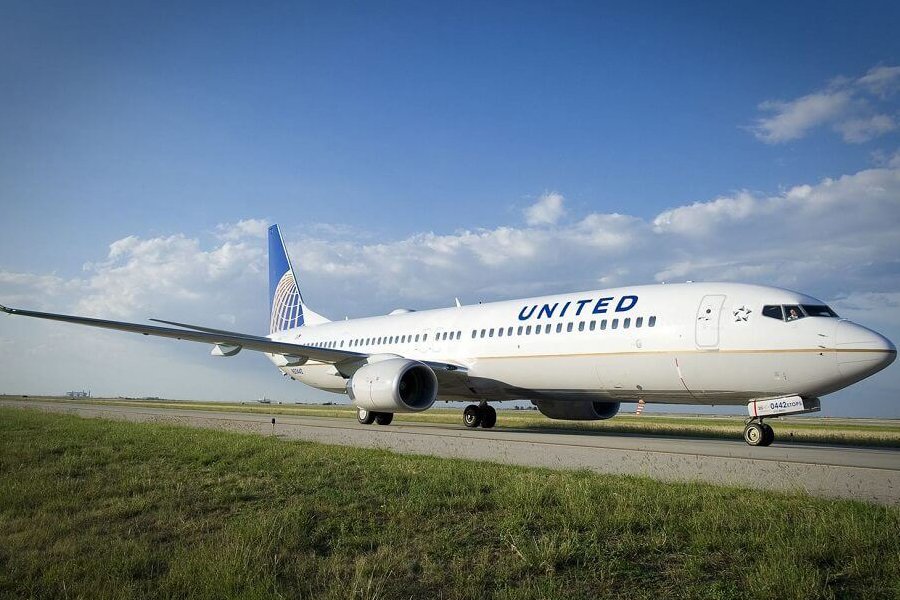 A United Airlines airplane, showcasing its white fuselage and iconic blue tail fin adorned with the golden globe logo, is positioned on a taxiway surrounded by green grass under a clear blue sky. The aircraft appears ready for takeoff or parked after landing, emphasizing a serene and professional aviation setting.