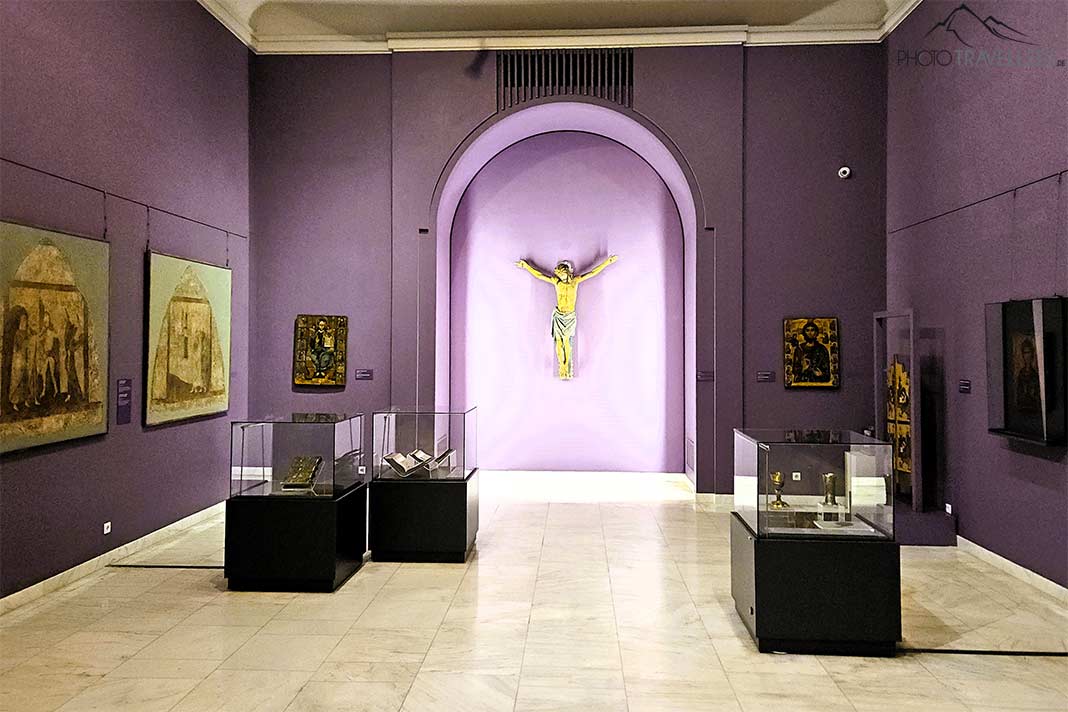 Lilafarbene Wände mit Bilder behangen und ein Jesuskreuz zieren einen Raum im Kunstmuseum in Bukarest