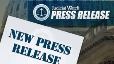 Judicial Watch press release with "NEW PRESS RELEASE" in large blue letters, against a backdrop of a government building. Judicial Watch logo with scales of justice is visible.