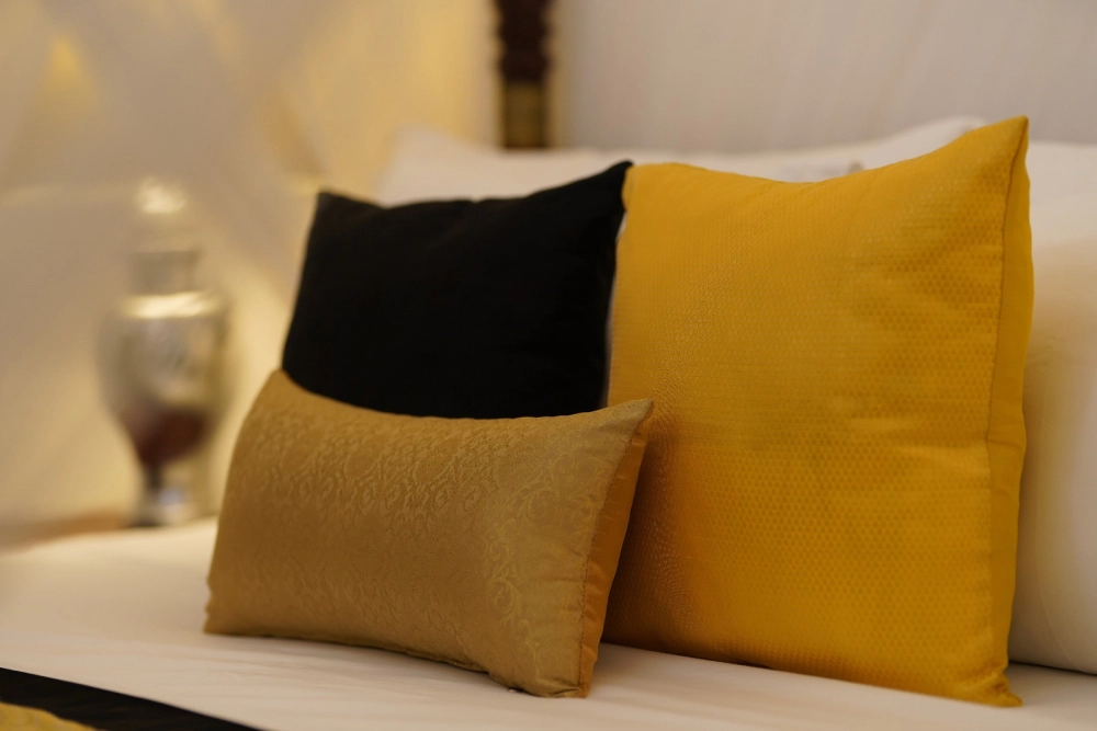 A cozy bed with decorative pillows, including a striking black and gold pillow, in the Lime Butterfly room at Adigar's Manor.