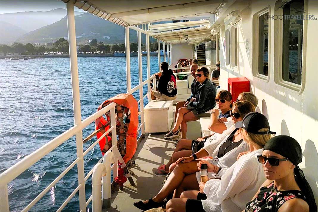 Eine Reihe von Menschen sitzt auf dem sonnigen Seitendeck einer kleinen Fähre