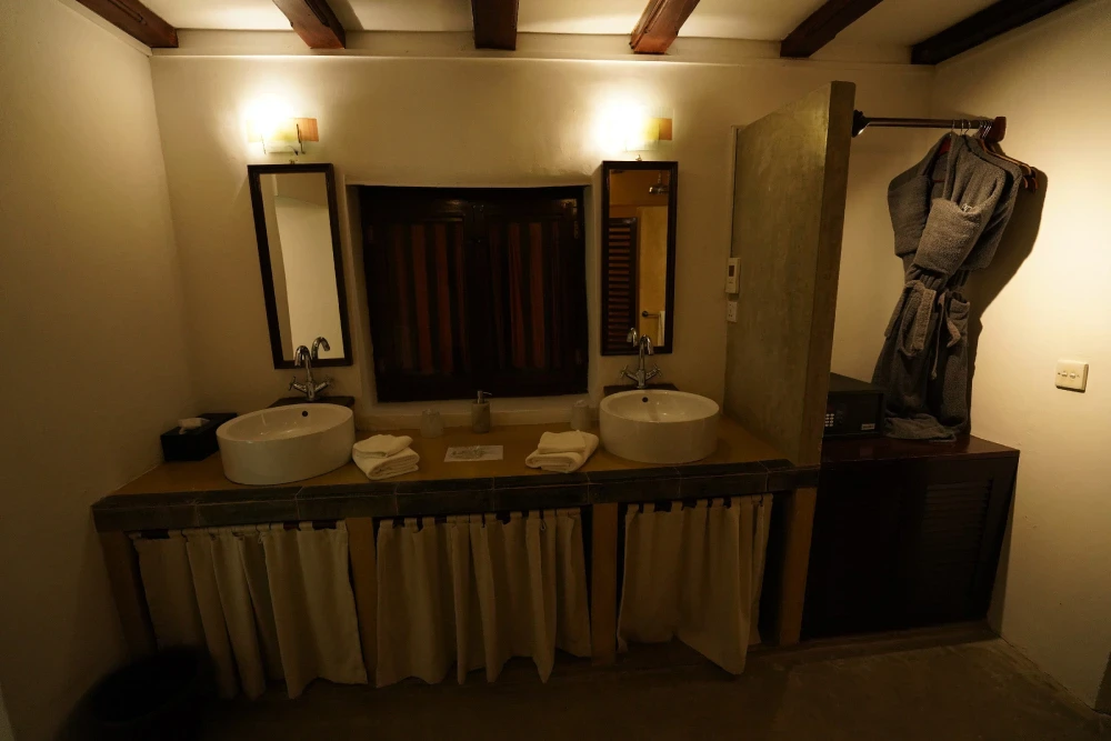 A bathroom in the monkey puzzle room of Adigar's Manor, featuring two sinks and robes hanging on the wall.