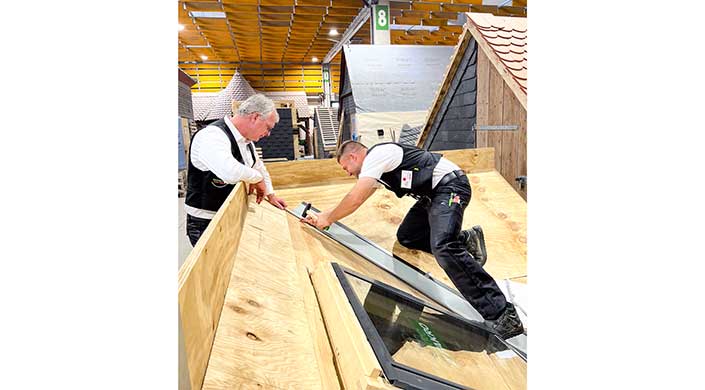Ein Handwerker misst und installiert ein Fensterrahmen auf einer Baustelle mit Holzboden in einer Werkstattumgebung.