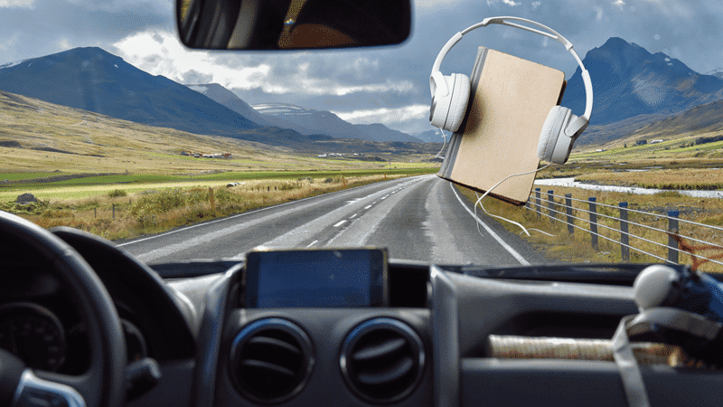 Car on Road and Book with Headphones / The Best Audio Books for Your Next Road Trip