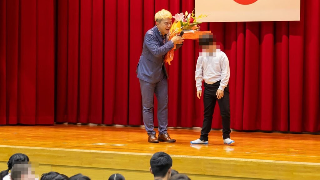 【PTA講演会 人気講師の選び方】「面白かった!」と言われる小学校・PTA講演会の3つの条件【2026年版】 6 高岡支援学校の創立60周年記念マジックショー後、生徒代表から笑顔で花束を受け取るマジシャン・コンプレッサー