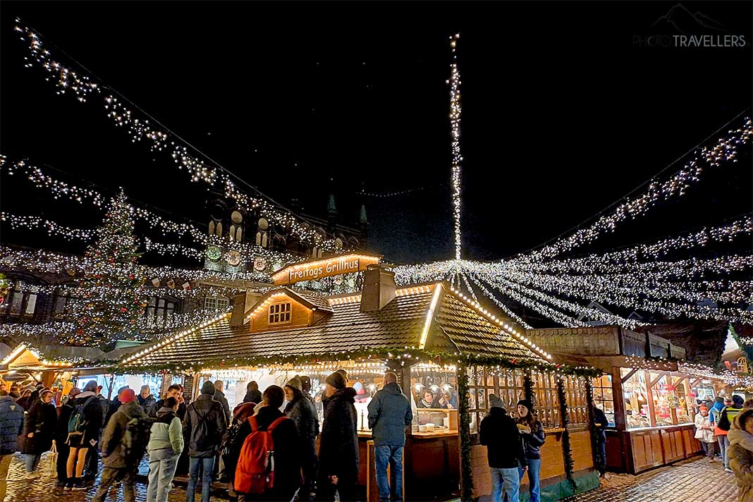 Menschen stehen an den Ständen des Lübecker Weihnachtsmarkt, der von hellen Lichtergirlanden illuminiert wird