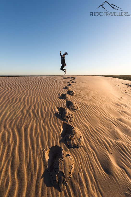 Reisebloggerin Biggi Bauer springt auf der Wanderdüne Råbjerg Mile in die Höhe. Vor ihr sieht man tiefe Fußspuren im Sand