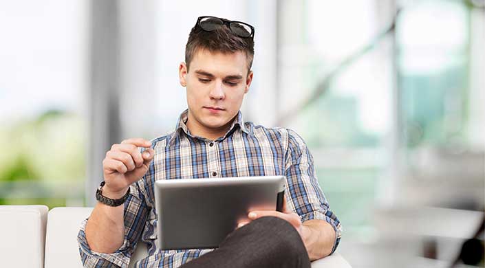 Ein junger Mann mit kariertem Hemd und Brille auf dem Kopf sitzt und benutzt ein Tablet.
