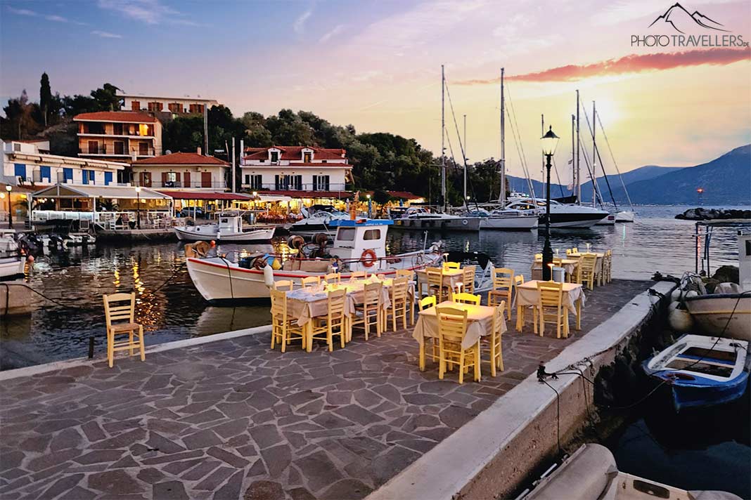 Stühle einer Taverne stehen im Sonnenuntergang neben Booten im Hafen von Vathi auf Methana