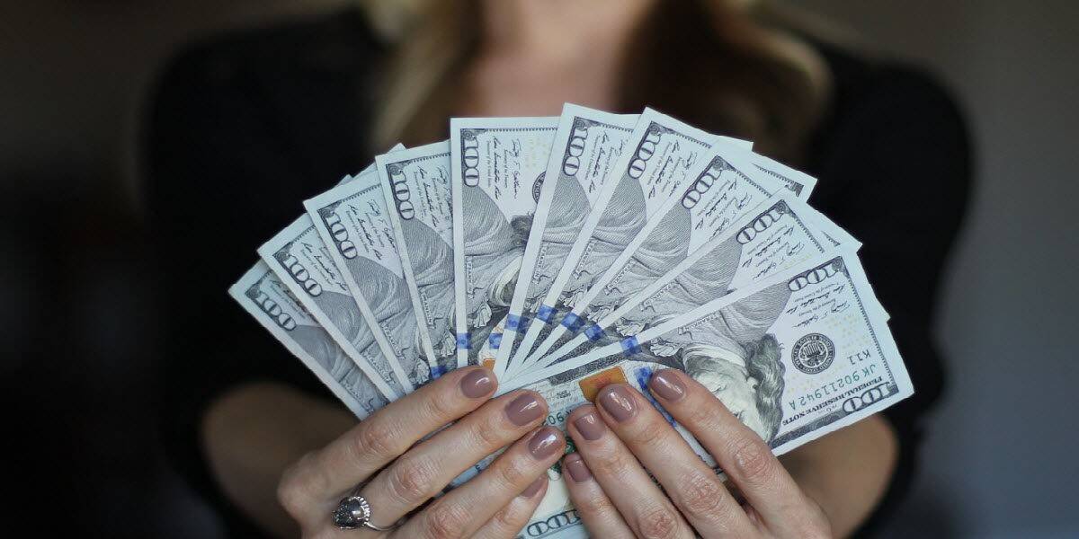 Person holding a fan of hundred-dollar bills, symbolizing cash rewards and SPIFF sales incentives.