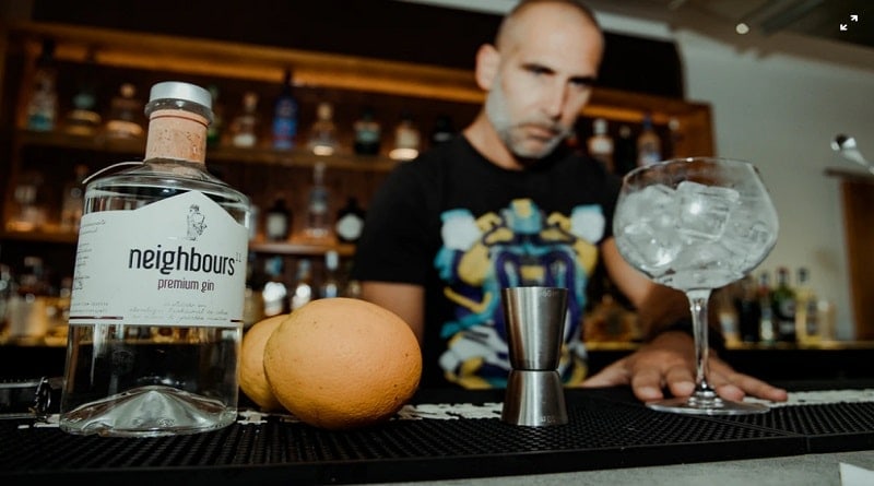Bartender behind bar with bottle of gin , oranges, and glass with ice - Gin Bar Ideas that Will Help Your Customers Get the Best Drinking Experience