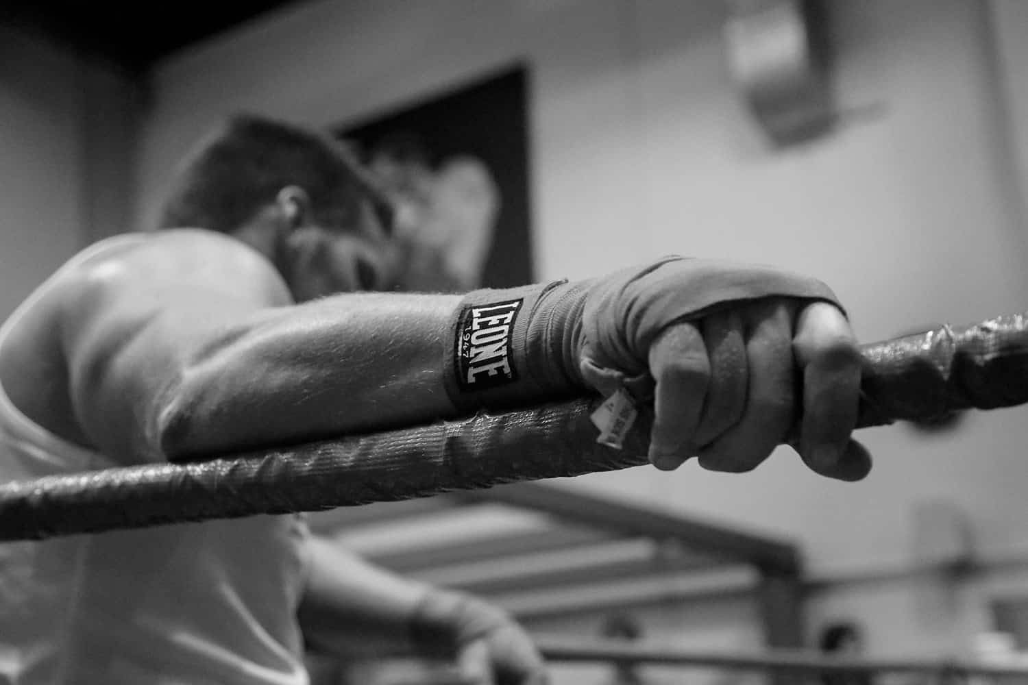 In our elite Dubai gym, a focused boxer with Leone wraps rests on the ropes—black-and-white dedication to top-tier training.