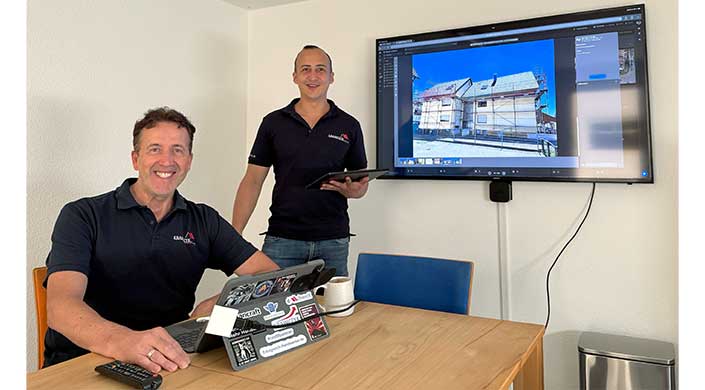 Bild von Karl-Heinz Krawczyk mit seinem Nachfolger Edgar Kümmerle Ein Mann steht in einem Büro, hält ein Tablet und lächelt neben einem Bildschirm, auf dem ein digitales Bild angezeigt wird. Ein Laptop und eine Tasse stehen auf dem Tisch.