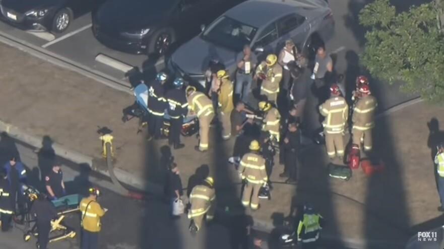 Emergency responders attend to injured victims after a small plane crash in Southern California near a warehouse. Firefighters and paramedics are visible at the scene, providing emergency aid following the Fullerton incident. FOX 11 News logo is visible.