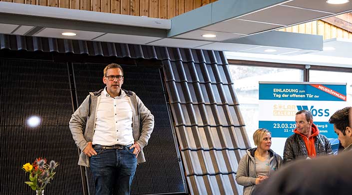 Mann steht neben einem mit Solarpaneelen ausgestatteten Dach und einem modern gestalteten Dachraum, teilweise sichtbar.