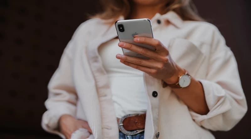 Woman in jeans a while shirt and cream color sweater holding a smart phone in her hand
