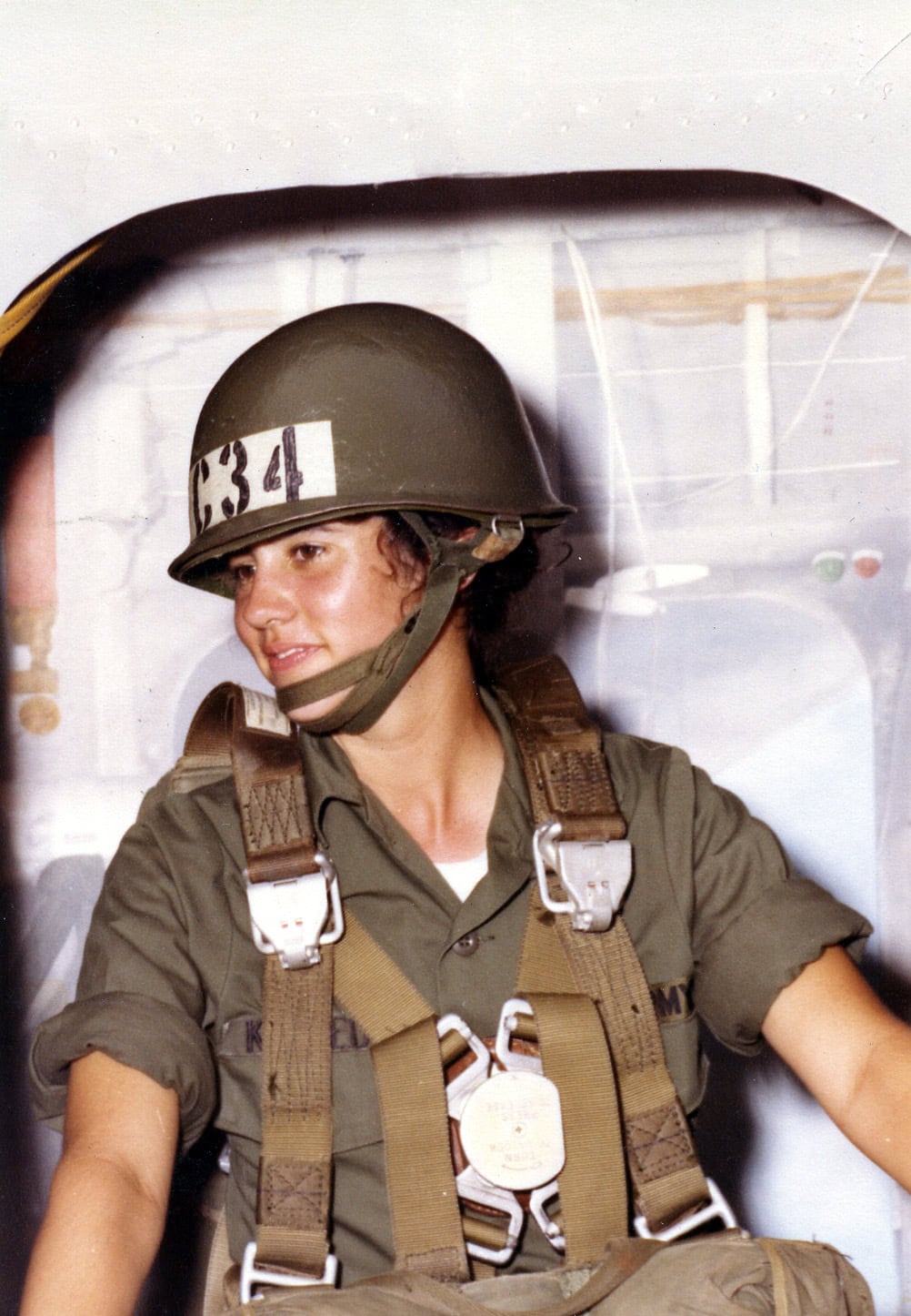 Mary Kennedy Thompson in military jump gear and helmet seated inside an aircraft during airborne training