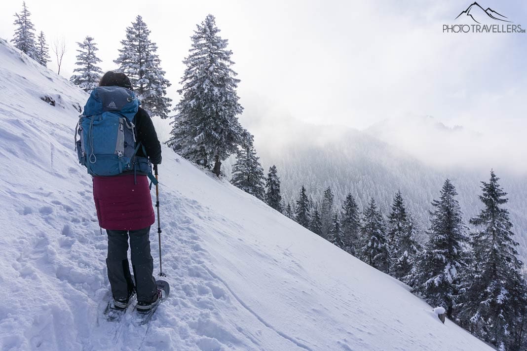 Reisebloggerin biggi Bauer mit Rucksack und Schneeschuhen in der verschneiten WiAufstieg zur Hochries mit Schneeschuhen
