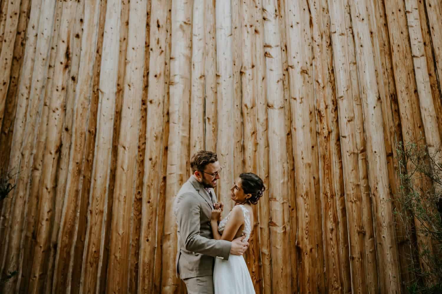 Brautpaar lächelte lächelnd an Holzfassade, Blick voller Liebe – Hochzeitsfotografin Köln Moment.