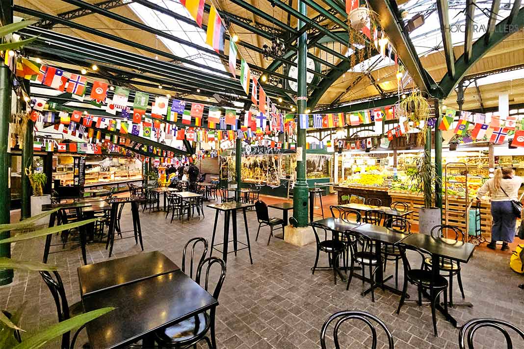 Leere Tische stehen vor den bunten Verkaufsständen in der Markthalle Saint Quentin
