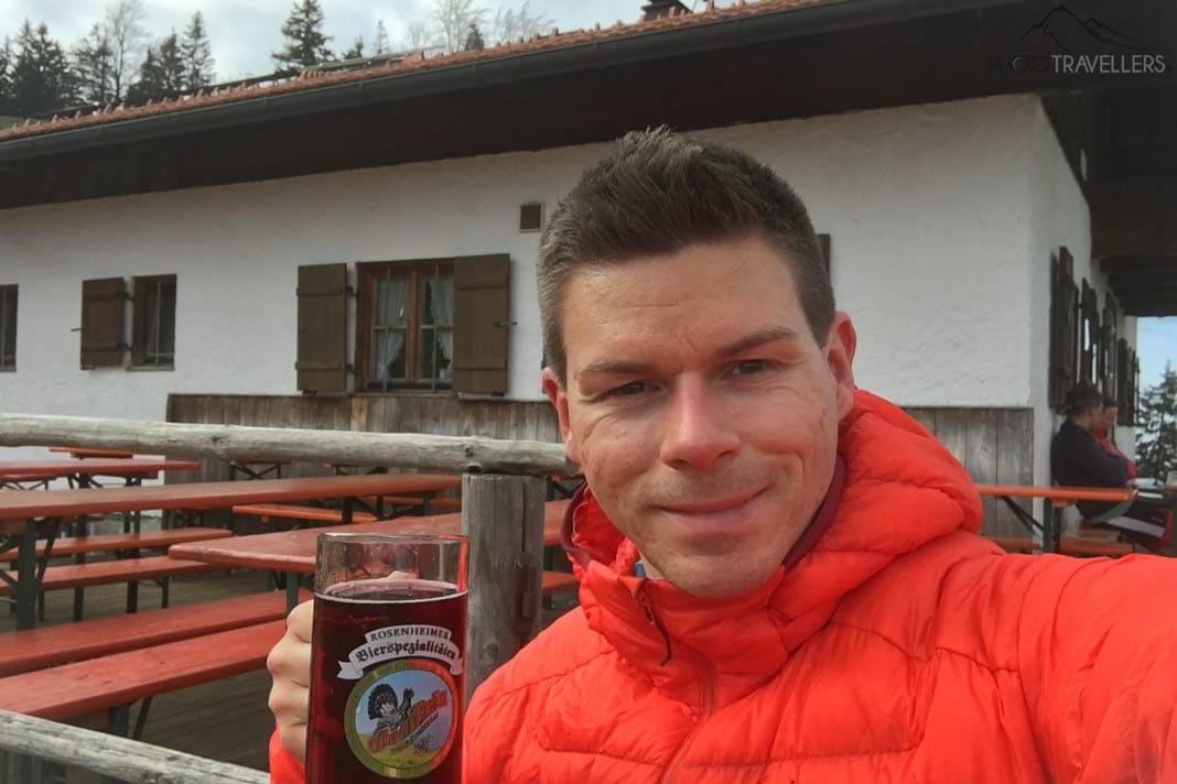 Reiseblogger Florian Westermann im Winter in einer orange Daunenjacke mit einer Saftschorle vor der Deindlalm