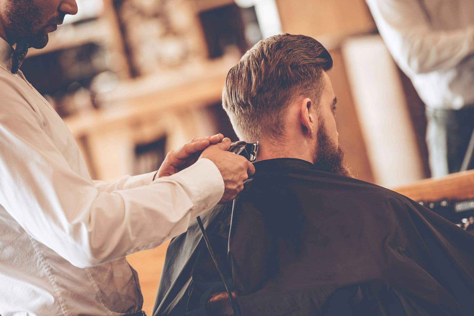 Barber uses clippers to trim the back of a man’s hair in a barbershop; illustrative image for Veterans Day free haircuts.