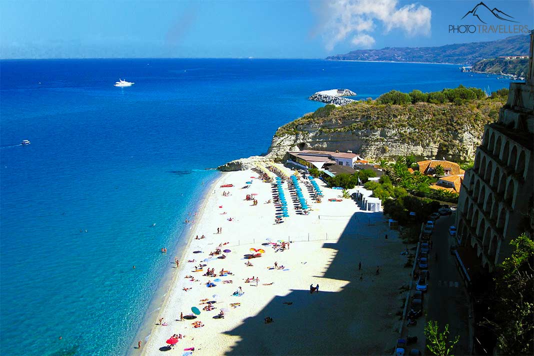 Blick von oben auf den weißen Sandstrand von Tropea mit hellblauen Sonnenschirmen und Badegästen