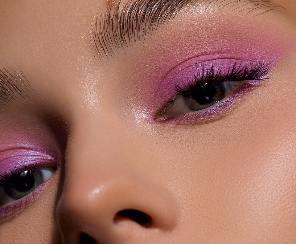 Detailansicht eines geschminkten Auges mit pinkem Lidschatten und langen Wimpern.