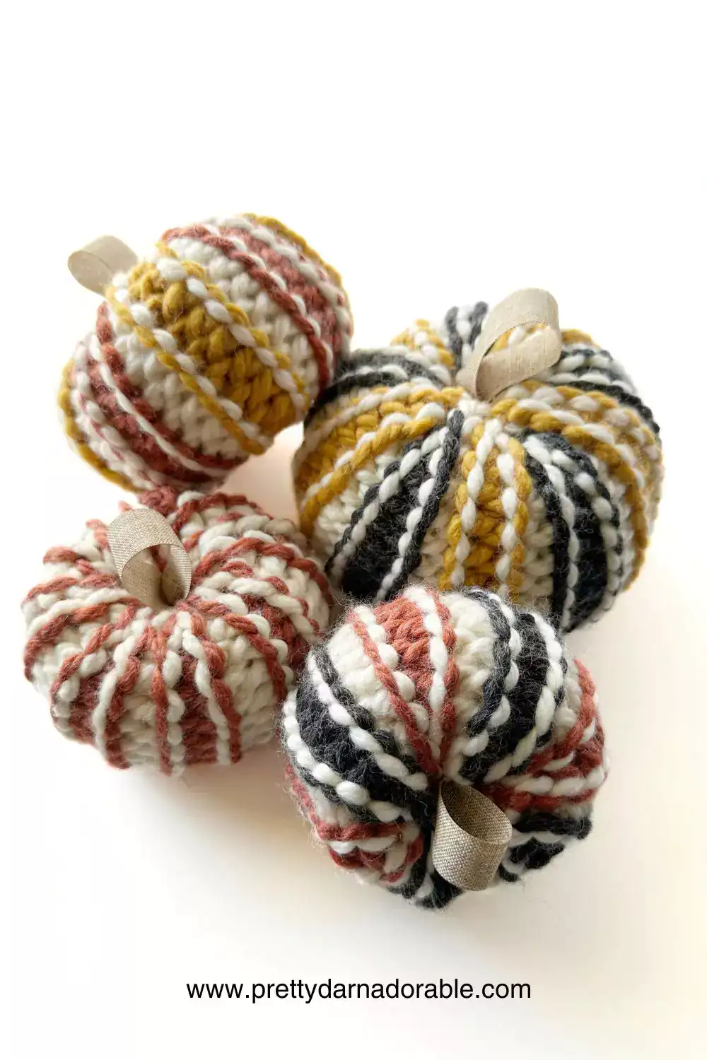 Four small, chunky ribbed crochet pumpkins in cream, yellow, black, and rust stripes on a white surface; free pattern at prettydarnadorable.com. Free crochet pattern