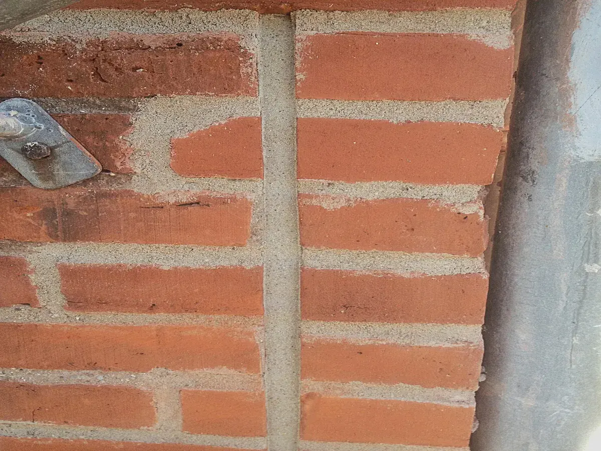 Sandbestrøet gummifuge som dilatationsfuge i murværk – matcher facade og fugefarve i teglbyggeri.