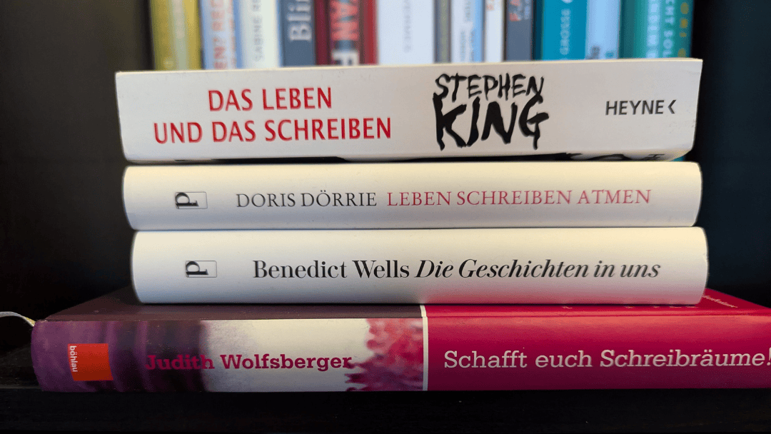 Ein Stapel inspirierender Bücher über das Schreiben, darunter Werke von Benedict Wells, Stephen King, Doris Dörrie und Judith Wolfsberger, auf einem Schreibtisch