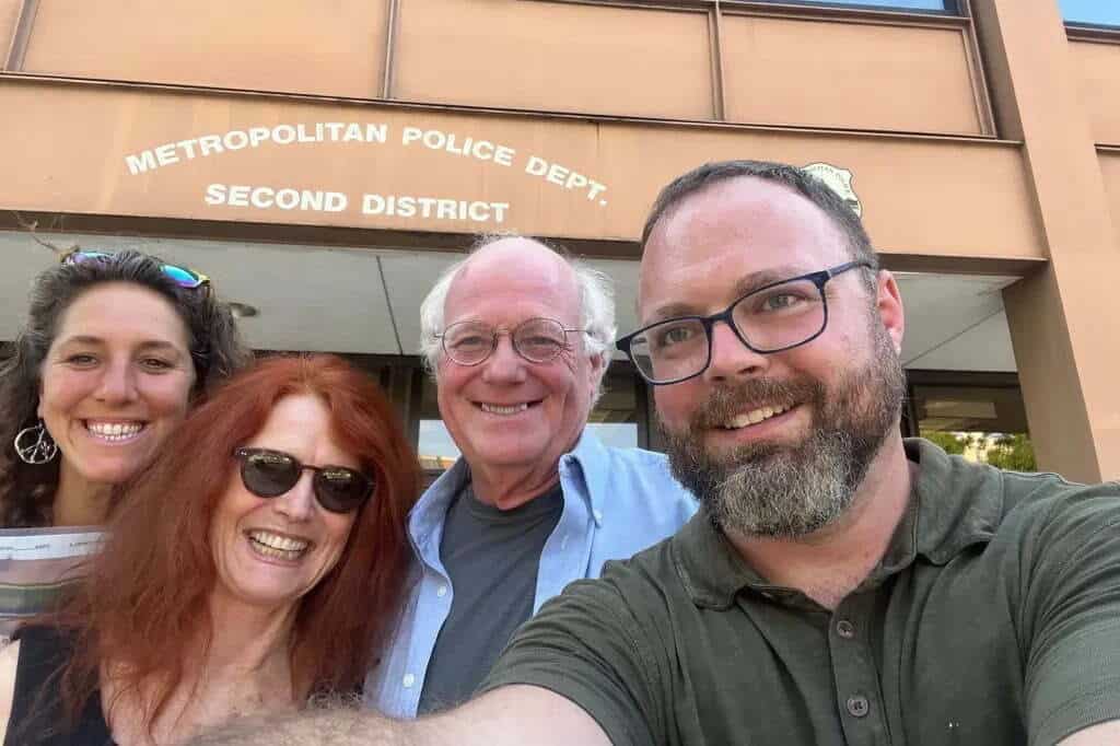 Ben Cohen, co-founder of Ben & Jerry's, smiles with fellow activists in front of the Metropolitan Police Dept. Second District. The group is likely participating in a Julian Assange protest, advocating for press freedom in DC.