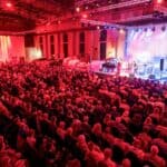 Ein Foto einer großen Menschenmenge die einem Konzert in der Halle lauschen.