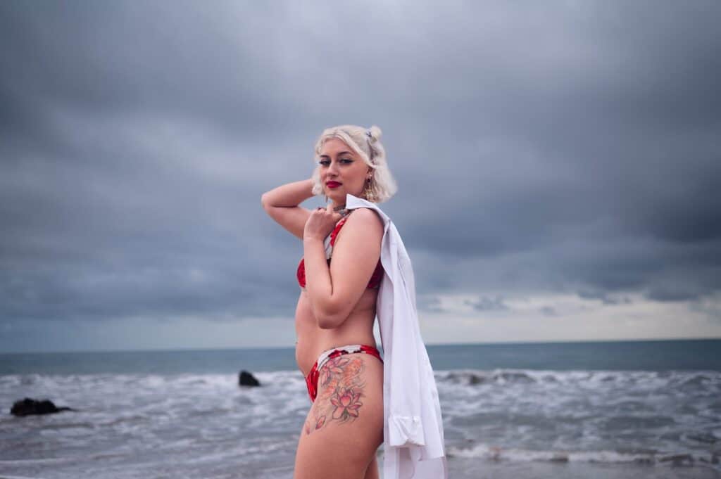 luxury boudoir photoshoot at el matador beach in los angeles. In this photograph the client is posing in a red and white bikini with a white button down thrown over her shoulder.