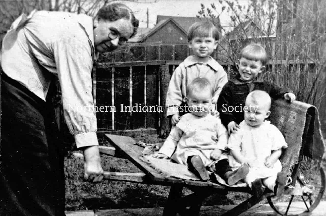 children in a wheelbarrow c. 1920s 1930s ph YPOH Szymanski (1) Childhood outdoor playing with woman and kids in backyard, vintage black and white photo.