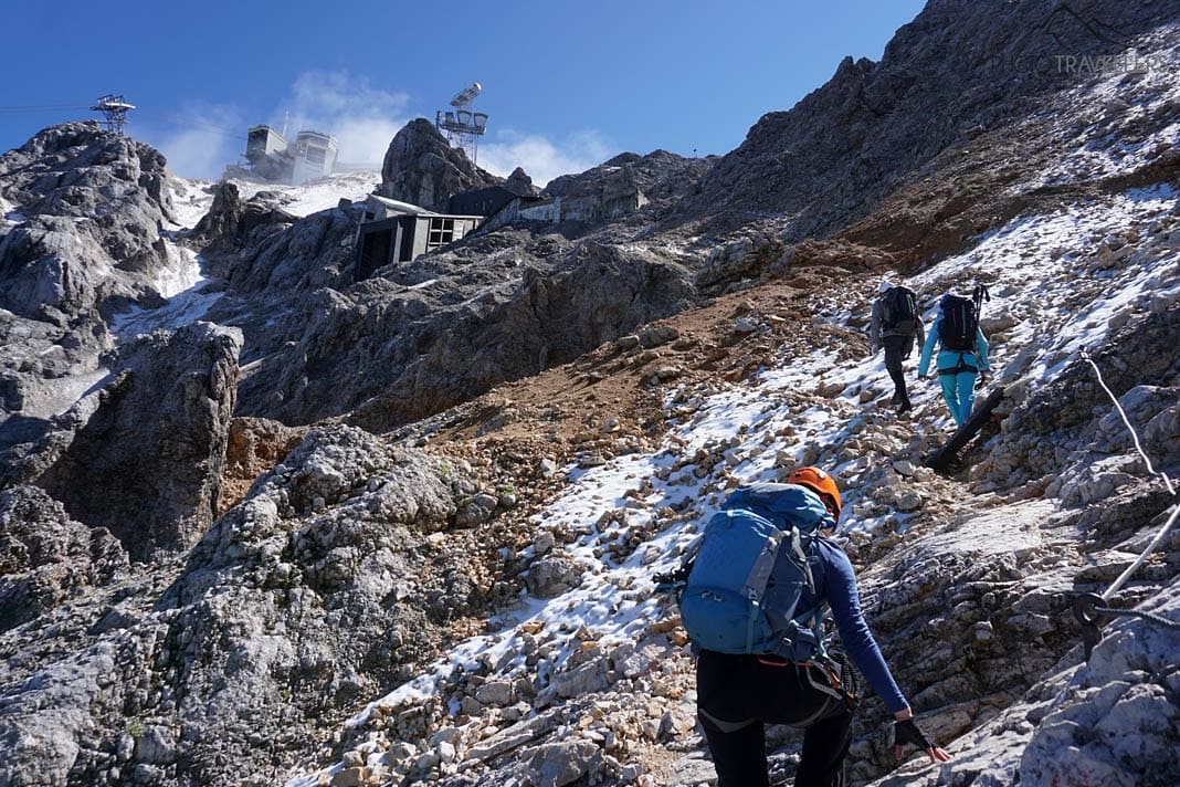Reisejournalistin Biggi Bauer und zwei Wanderer vor der alten und neuen Bergstation der Tiroler Zugspitzbahn