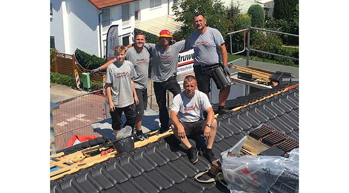 Vier Männer in grauen T-Shirts posieren zusammen auf einem Dach, einer sitzt, drei stehen, im Hintergrund ist ein Firmenbanner zu sehen.